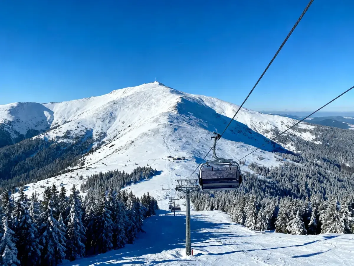 Zimowa panorama ośnieżonych stoków Kopy w Karkonoszach z widocznym wyciągiem krzesełkowym na tle błękitnego nieba.