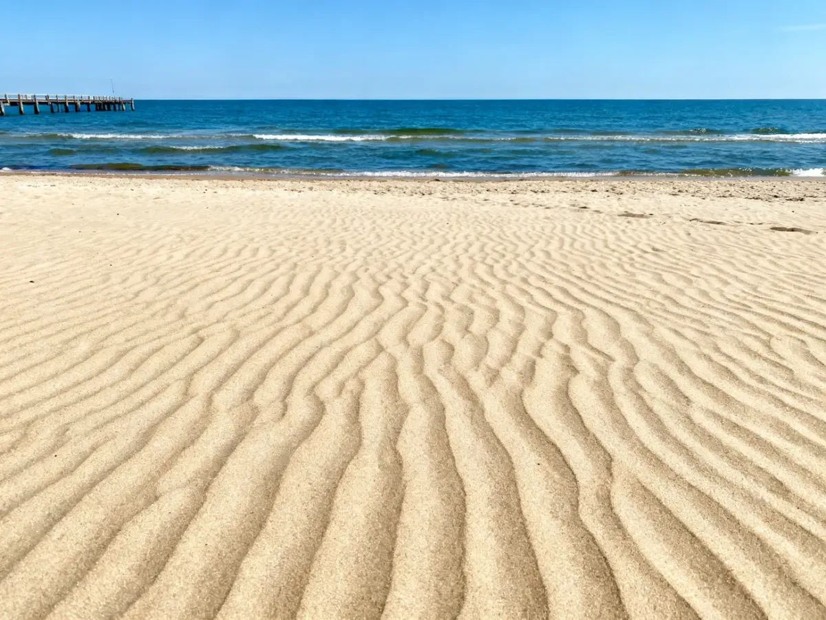 Słoneczna plaża w Chłopach z widokiem na spokojne morze i drewniane molo w letni dzień.